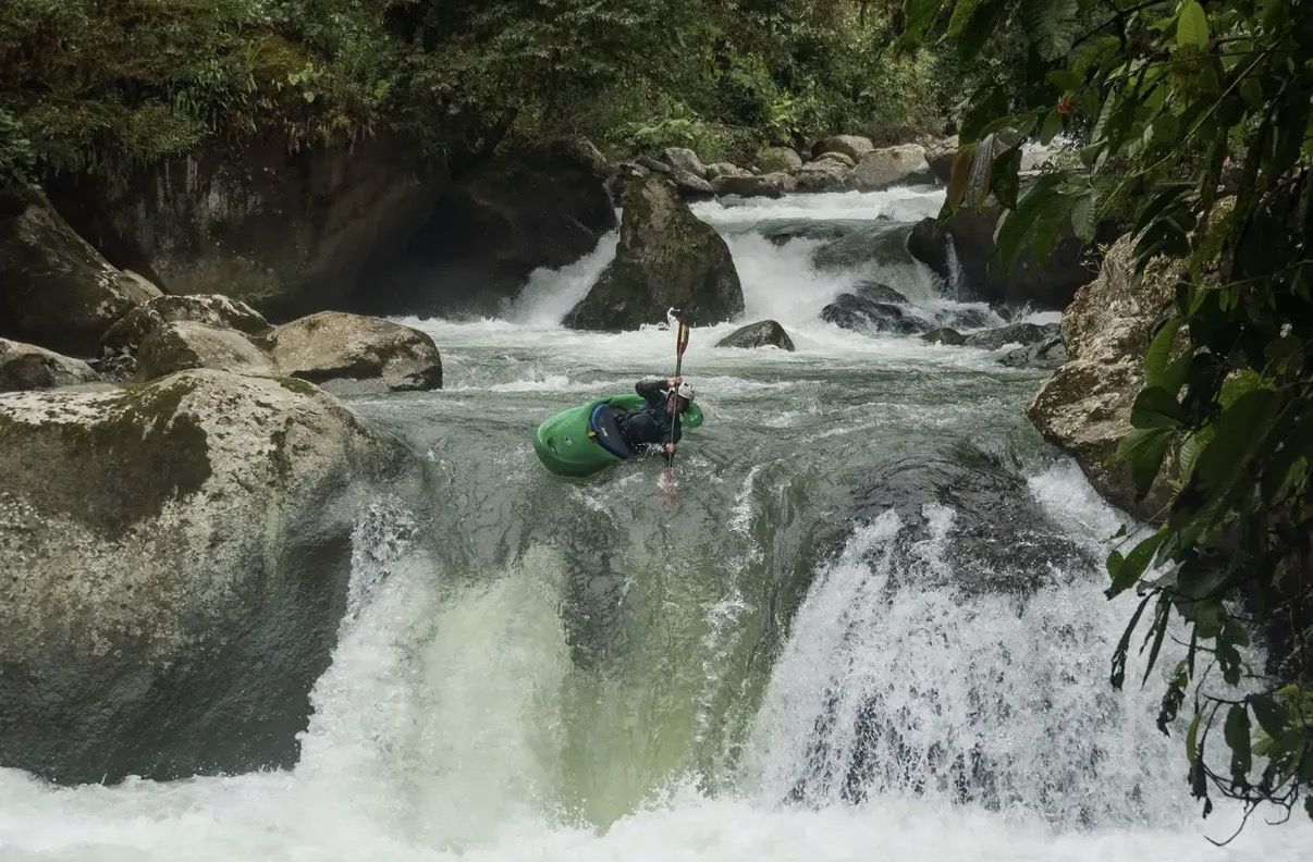 A kayaker in a green boat lines up at the lip of a waterfall