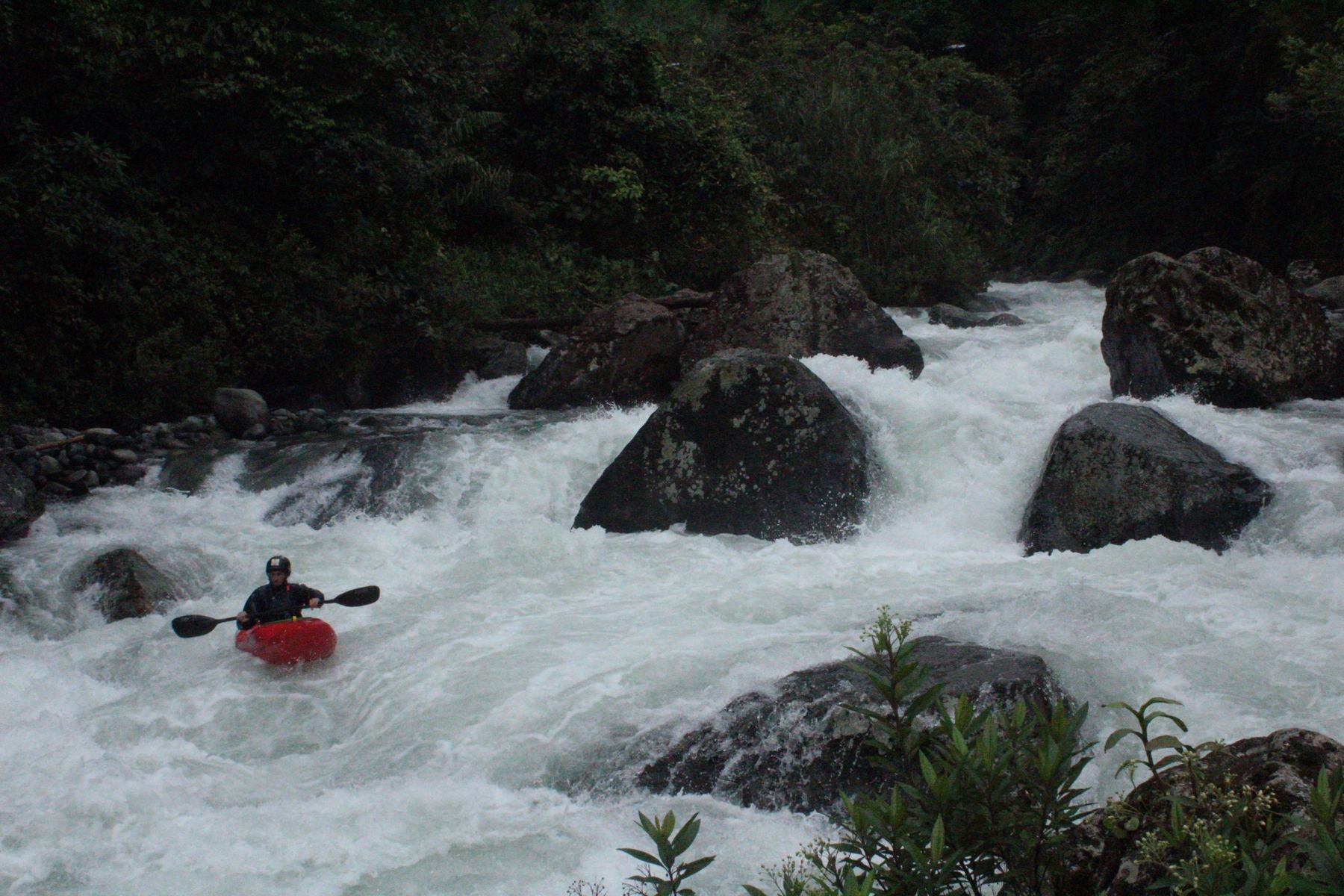A kayaker in a red boat in big whitewater between boulders
