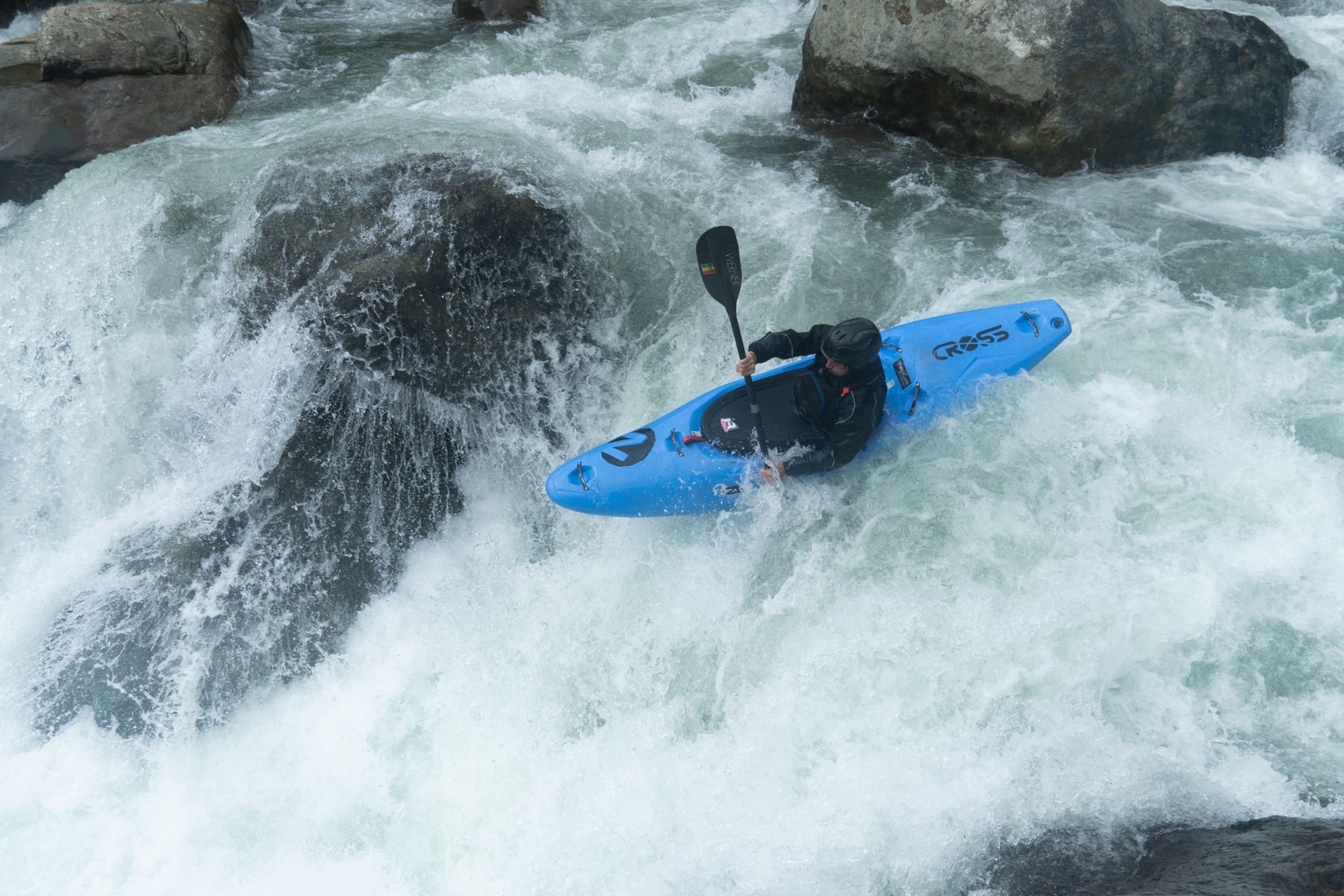 A kayaker in a blue creek boat in a powerful rapid