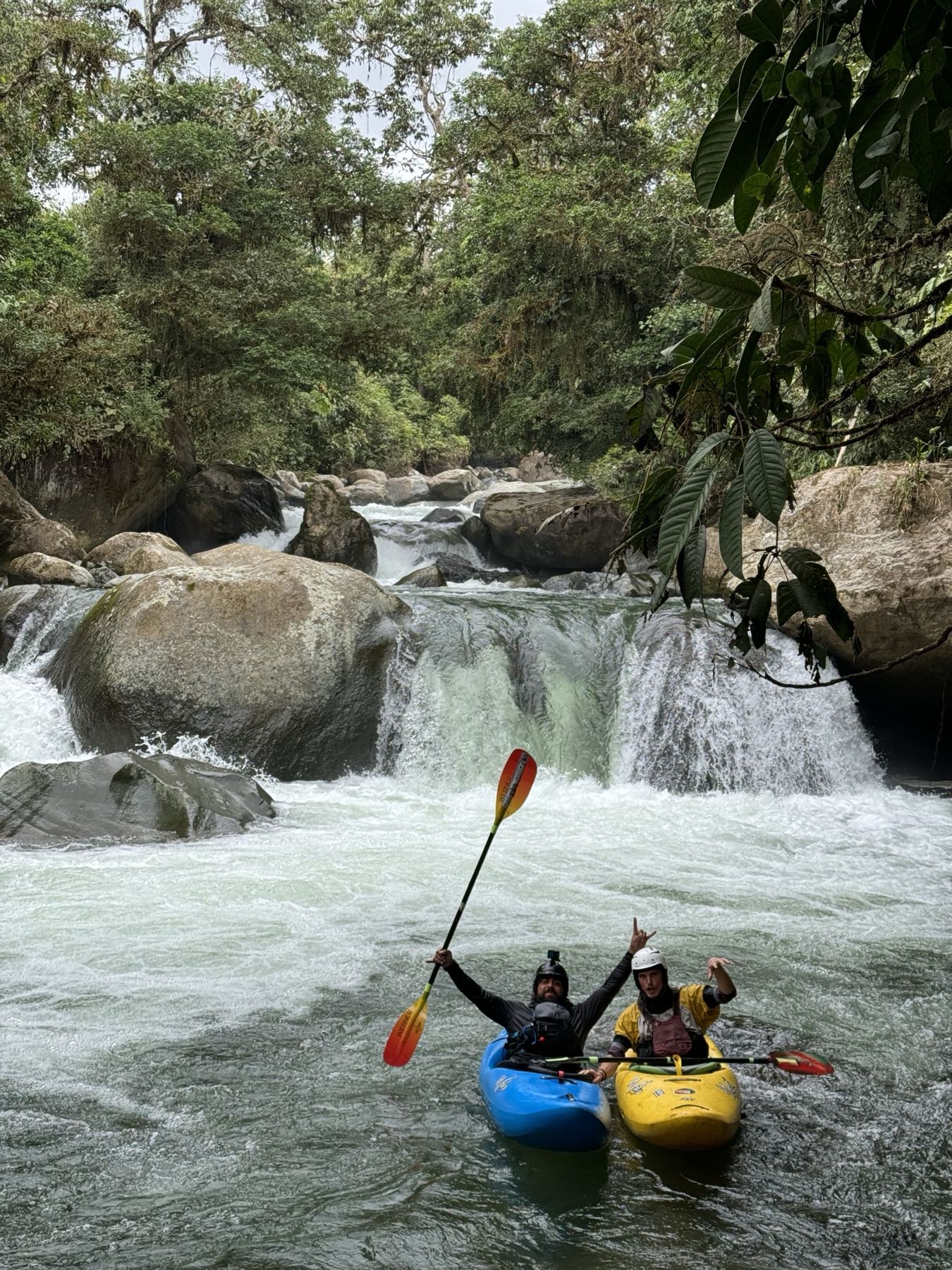 Two kayakers celebrate below a waterfall